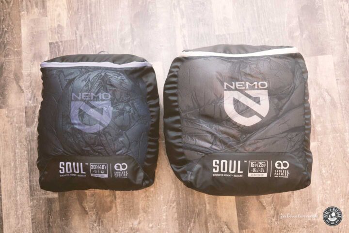 Zwei NEMO Kunstfaserschlafsäcke im Packsack auf Holzboden.