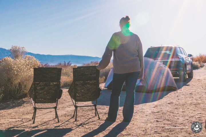 Frau steht neben Helinox Chairs auf Campingplatz mit Zelt und Auto.