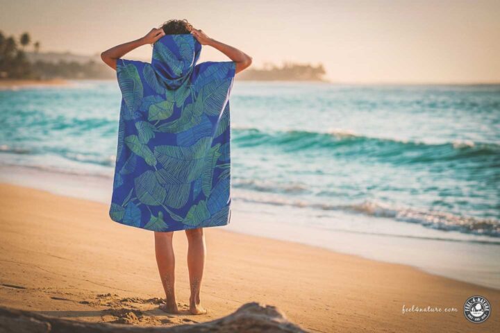 Frau mit Handtuch-Poncho am Strand.